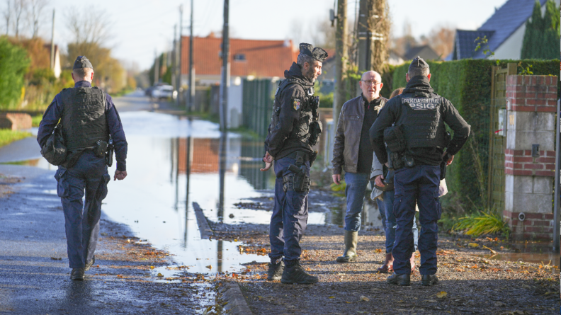 En extérieur, de jour, deux gendarmes échangent avec des habitants pendant qu'un autre militaire se rend dans la zone inondée.
