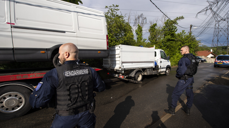 Deux gendarmes observent une dépanneuse remorquant une camionette.