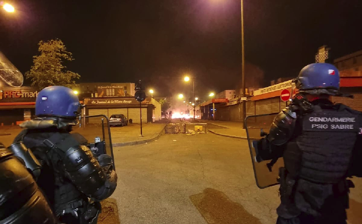 Des militaires du PSIG SABRE avec leurs protections et leurs boucliers progressent dans une rue où des barricades ont été enflammées.