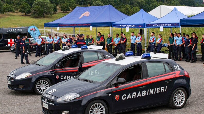 Au premier plan, des voitures de carabiniers italiens sur la piste. Au second, les stagiaires écoutent un cadre italien qui explique l'exercice.