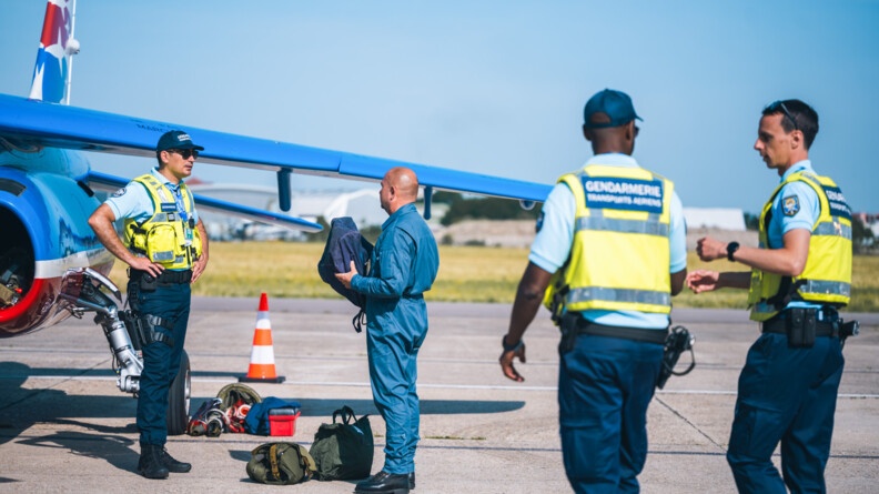 Trois gendarmes de la GTA et un personnel de la patrouille de France, auprès d'un avion de la PAF sur le tarmac