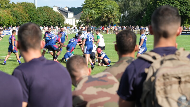 Match de rugby avec des militaires spectateurs au premier plan de dos