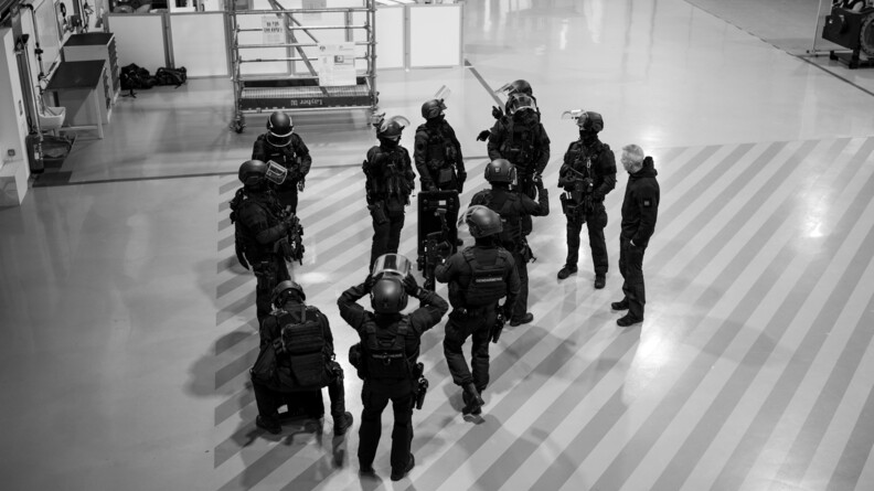 Des gendarmes du PSPG en tenue d'intervention et armés, écoutent le briefing de leur chef. Ils sont dans une salle en intérieur.