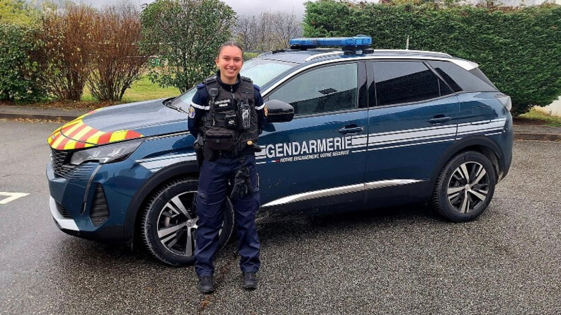 La gendarme Maëlys en tenue d'intervention devant un véhicule sérigraphié de la gendarmerie.
