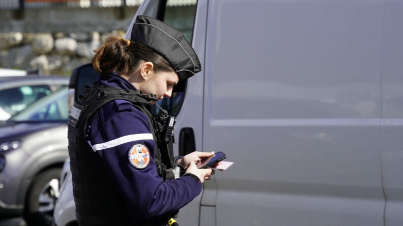 Une gendarme en train de passer au fichier un permis de conduire devant un van gris