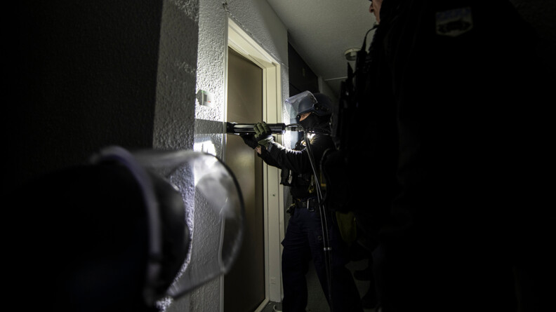 Un groupe de gendarme qui s'apprêtent à inspecter une porte. L'un d'entre eux tiens une lampe de torche et essaie d'ouvrir la porte.