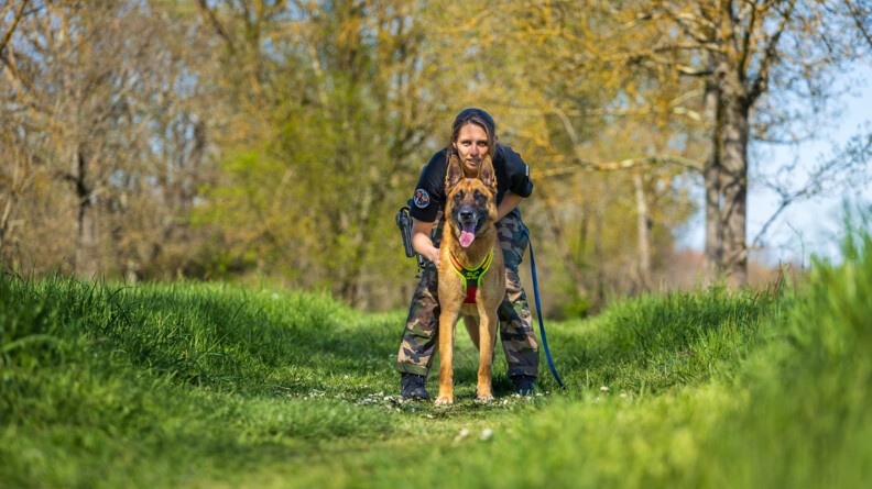 L'adjudante Mélanie et son chien Looba, dans un champ, sous les arbres, face objectif.
