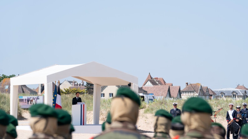 Le président de la République prononce l'hommage national à son pupitre habillé du drapeau bleu blanc rouge, et sous une tente blanche. Au premier plan, de dos, des fusiliers marins de la Marine nationale.