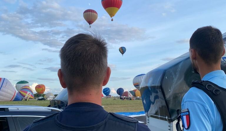 Un polizei allemand et un gendarme français de l'UOFA vus de dos, observant les abords de l'aérodrome, d'où décollent des montgolfières.