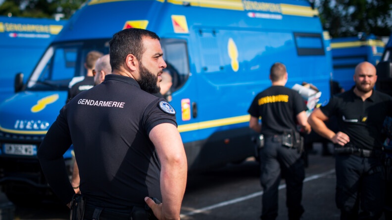 Un gendarme de dos devant un nouveau VCT de la gendarmerie nationale. A droite deux autres gendarmes en flou, un de dos, un de face.