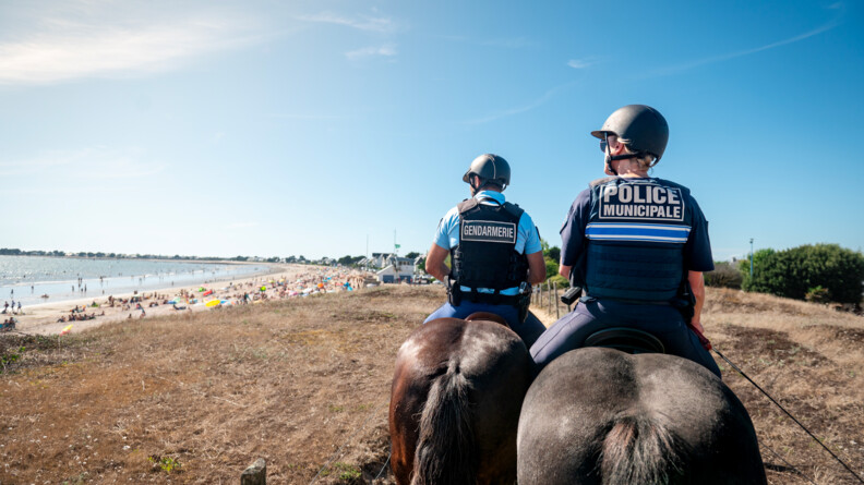 Un gendarme et une policière municipale (de dos) surveillent une plage à cheval.
