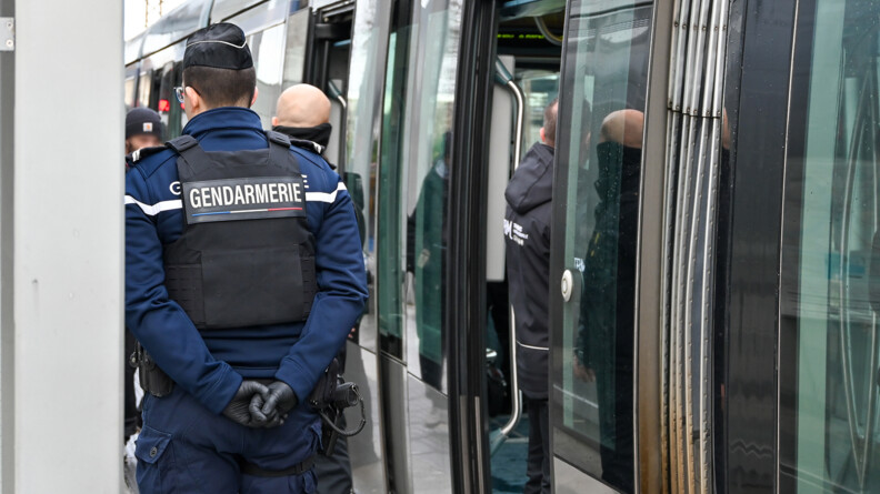 Photo d'un gendarme de dos. Il a les mains croisées derrière le dos. Il se trouve sur le quai à côté d'un train.