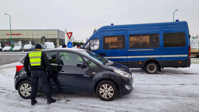 Des gendarmes contrôlent un véhicule bleu foncé. en arrière plan la ville et un camion de gendarmerie mobile