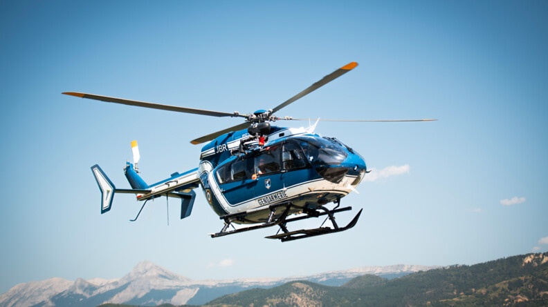 Un secouriste embarqué dans un hélicoptère gendarmerie survolant des montagnes.