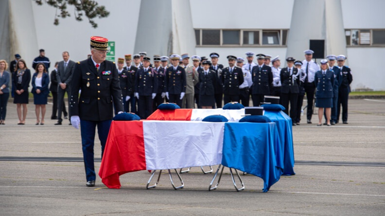 Le directeur général de la gendarmerie, une main posée sur l'un des deux cercueils.