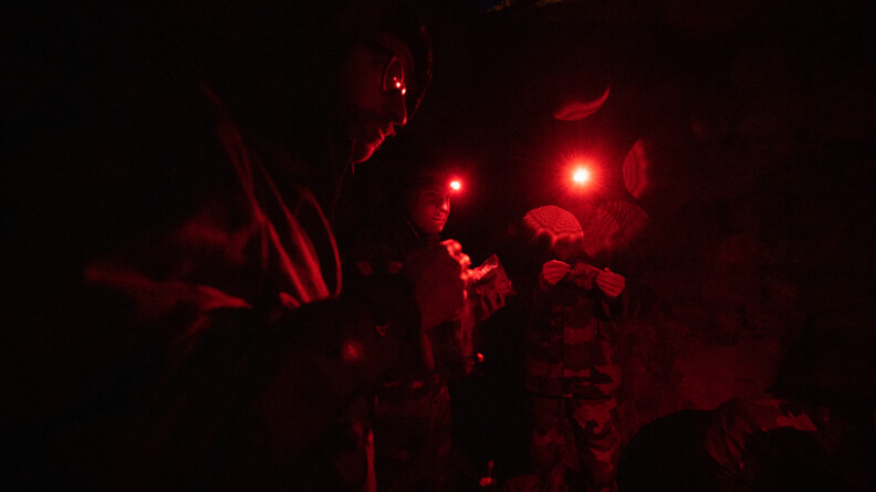 Trois miliciens, en cercle, s'éclairent avec des lampes rouges pour pouvoir manger leur ration