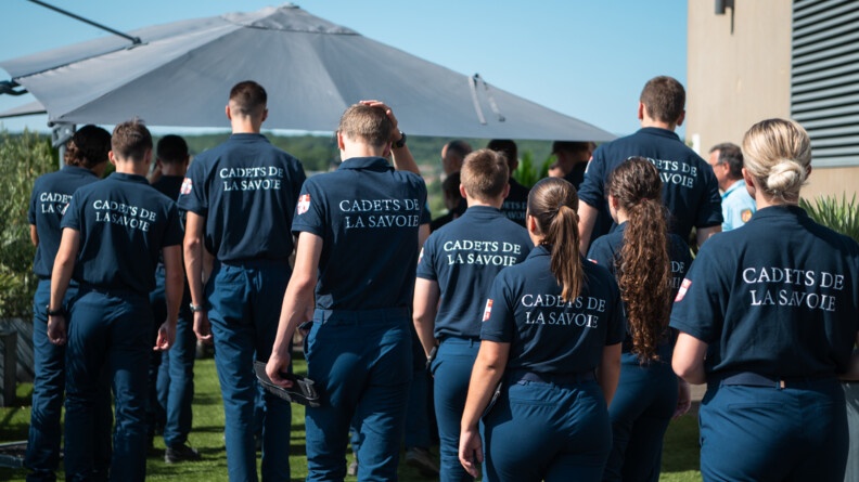 Une dizaine de cadets de SAvoie marchent, vu de dos, avec le polo noir siglé "cadets de la Savoie"