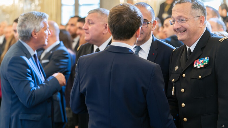 Le président de la République, de dos, échange avec le général d'armée Christian Rodriguez, à droite, et le préfet de police de Paris, à gauche. A gauche de l'image, en arrière-plan, le directeur des opérations et de l'emploi échange avec un homme en costume bleu.
