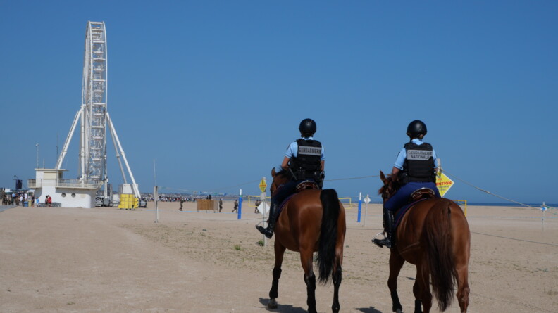 Deux gendarmes à cheval sur la plage qui s'avancent vers une grande roue.