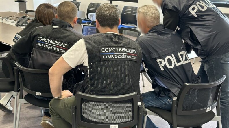 Trois enquêteurs du ComCyberGend et deux policiers étrangers devant un ordinateur.