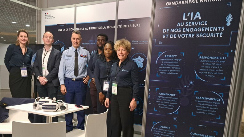 Les six personnels de la gendarmerie nationale, autour du général de brigade Patrick Perrot, chef du Service transformation (ST) de la Direction générale de la gendarmerie nationale (DGGN), et coordonnateur national de l’IA au sein de la gendarmerie, sur le stand de la gendarmerie nationale au World Artificial Intelligence Cannes festival (WAICF).
