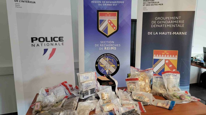 Plusieurs scellés contenant des stupéfiants (héroïne et résine de cannabis), de l'argent liguide et des armes sont posés sur une table, devant les kakémonos des trois unités d'enquête : la S.R. de Reims, la BSU (DDSP 52) et le GGD 52.