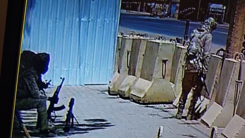 Capture de la vidéoprotecion de l'ambassade de France montrant deux soldats des RSF, lourdement armés (AK, RPK, RPG), effectuant des checkpoints aléatoires devant la résidence de l'ambassade française à Khartoum. Derrière eux, dans le fond, une palissade en tôle bleue,  et sur la droite, le long de la route, des blocs de béton.