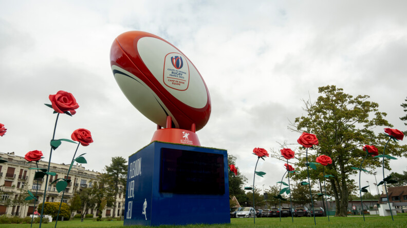 Ballon de rugby géant installé sur une pelouse, entouré de fausses roses géantes, au centre du rond point des sports au Touquet.