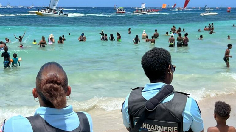 Deux gendarmes, de dos, sur la plage, surveillent la course nautique, ainsi que les spectateurs dans l'eau.