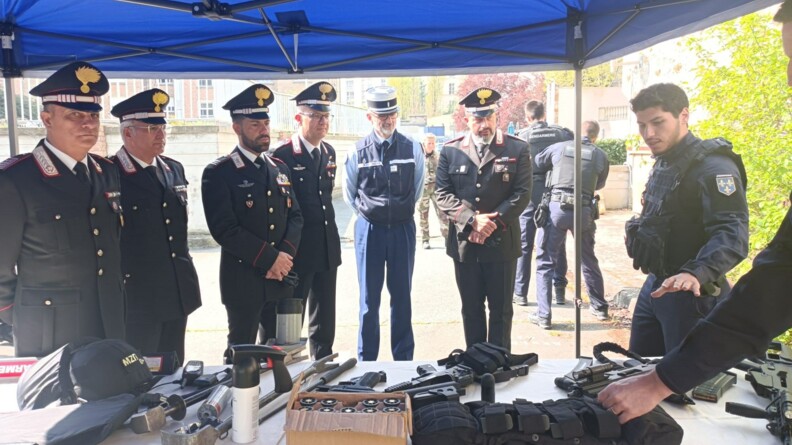 Cinq carabiniers en tenue et un colonel de gendarmerie devant une table où sont présentés l'équipement et l'armement du PSIG. A droite, un gendarme donne les explications.