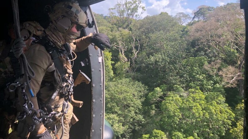 Un militaire du GIGN vu de profil, devant l'ouverture latérale d'un hélicoptère du GIH en vol au-dessus de la canopée, en forêt guyanaise.