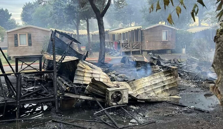 Photo montrant un mobil-home intégralement brûlé au premier plan et trois bungalows intacts en arrière-plan.