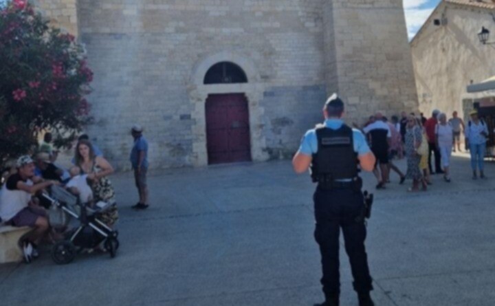 En extérieur, un gendarme surveillent la place devant l'église où de nombreux croyants se préparent à entrer.