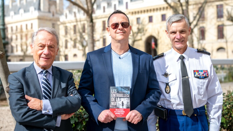 L'IGGN, l'auteur Marco Pianelli et le président des éditions PLON prennent une photo tous les trois, avec le quartier des Célestins en arrière plan, il fait beau et l'auteur tient son livre en main.