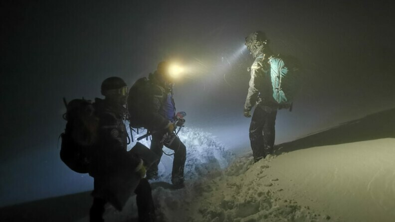 Trois gendarmes de PGHM dans la nuit et dans la neige avec des lampes torches.