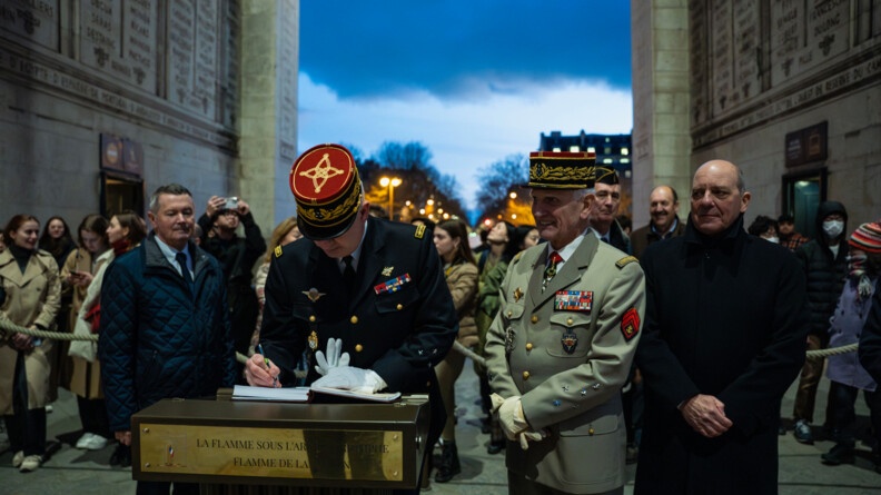 Un général de gendarmerie en train de signer le livre de la flamme. A ses côtés, un général de l'armée de Terre et deux homme en civil.