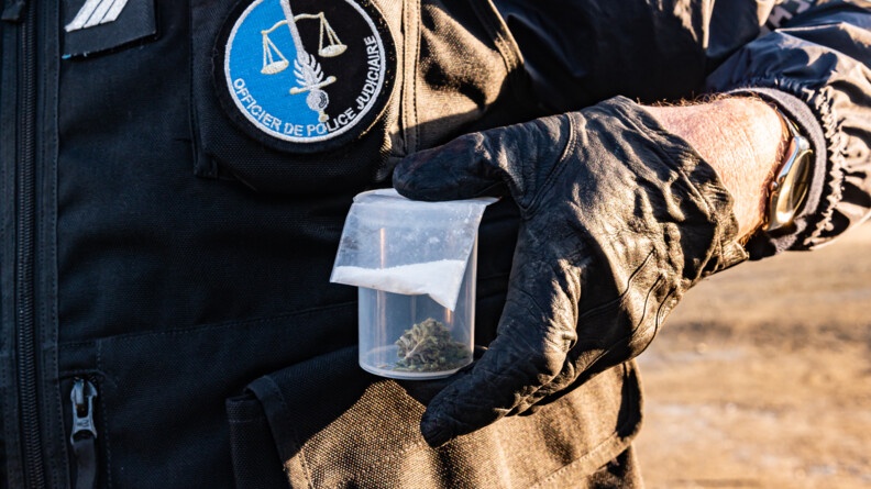 Un maréchal des logis-chef de gendarmerie tient un sachet de poudre blanche et un pochon de cannabis