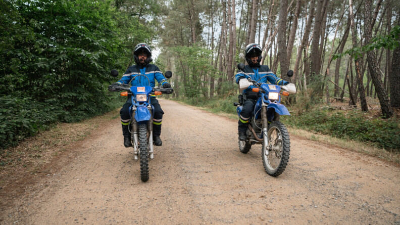 Sur une piste en terre dans la forêt, deux gendarmes roulent avec des motos tout terrain