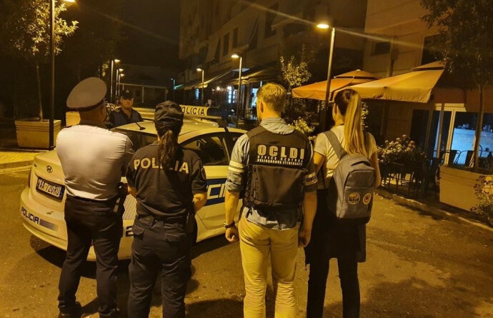 Opération judiciaire menée en Albanie par quatre enquêteurs, de dos devant une voiture de police albanaise, dont deux policiers albanais et un gendarme de l'OCLDI équipé d'un gilet pare balles.
