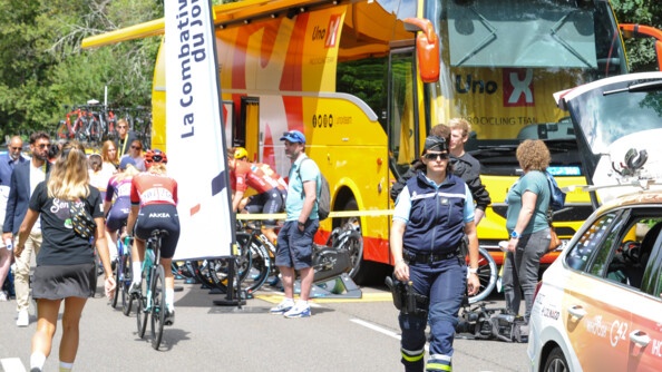 queue de peloton du Tour de France féminin, atelier de vélo avec un bus jaune et une gendarme marchant vers la droite