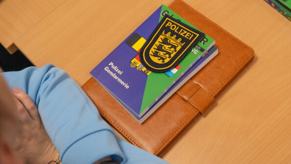 Nous voyons l'écusson Polizei avec le livre du lexique Polizei/Gendarmerie sur la table d'une jeune gendarme