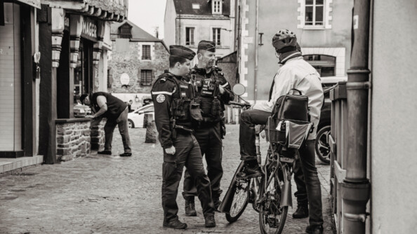 Deux gendarmes discutant avec un monsieur à vélo dans la rue.