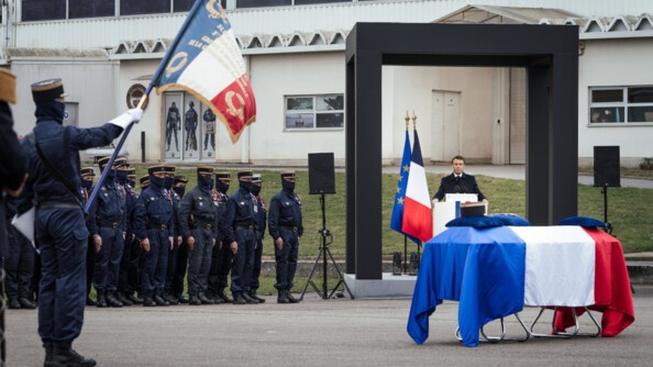 Au premier plan, le cercueil du major Arnaud Blanc, recouvert du drapeau français. Au second plan le président de la République, Emmanuel Macron, prononce le dicours d'hommage de la Nation, devant les militaires du GIGN.