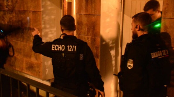 Trois gendarmes mobiles, dans la pénombre, devant les entrées d'un bâtiment.