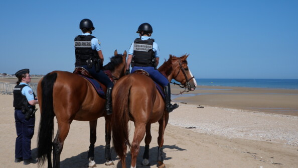 Deux gendarmes à cheval et une gendarme à pied, en mission de sécurisation sur la plage.
