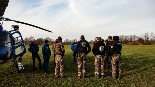 Une douzaine de gendarmerie en treillis et pull noir reçoivent un briefing au pied d'un hélicoptère de la gendarmerie situé à gauche