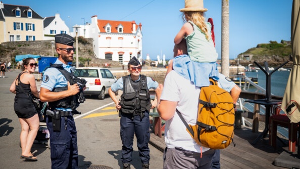 Deux gendarmes échangent avec un homme qui porte sa fille sur les épaules à Belle-Ile en Mer.