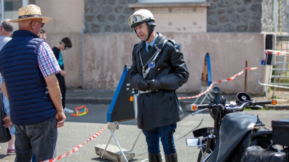 Un motard de la gendarmerie en tenue d'époque avec sa moto, au centre, échange avec un visiteur, à gauche.
