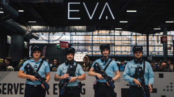 Dans un grabd hall d'exposition, quatre gendarmes gamers posent en tenue de gendarme, armés d'une arme de jeu. Tpus portent une casquette noire portant le sigle EVA.