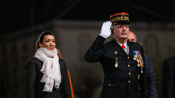 A gauche une femme en noir avec une écharpe blanche, les bras le long du corps, et le Directeur général de la gendarmerie nationale en vareuse, effectuant le salut militaire